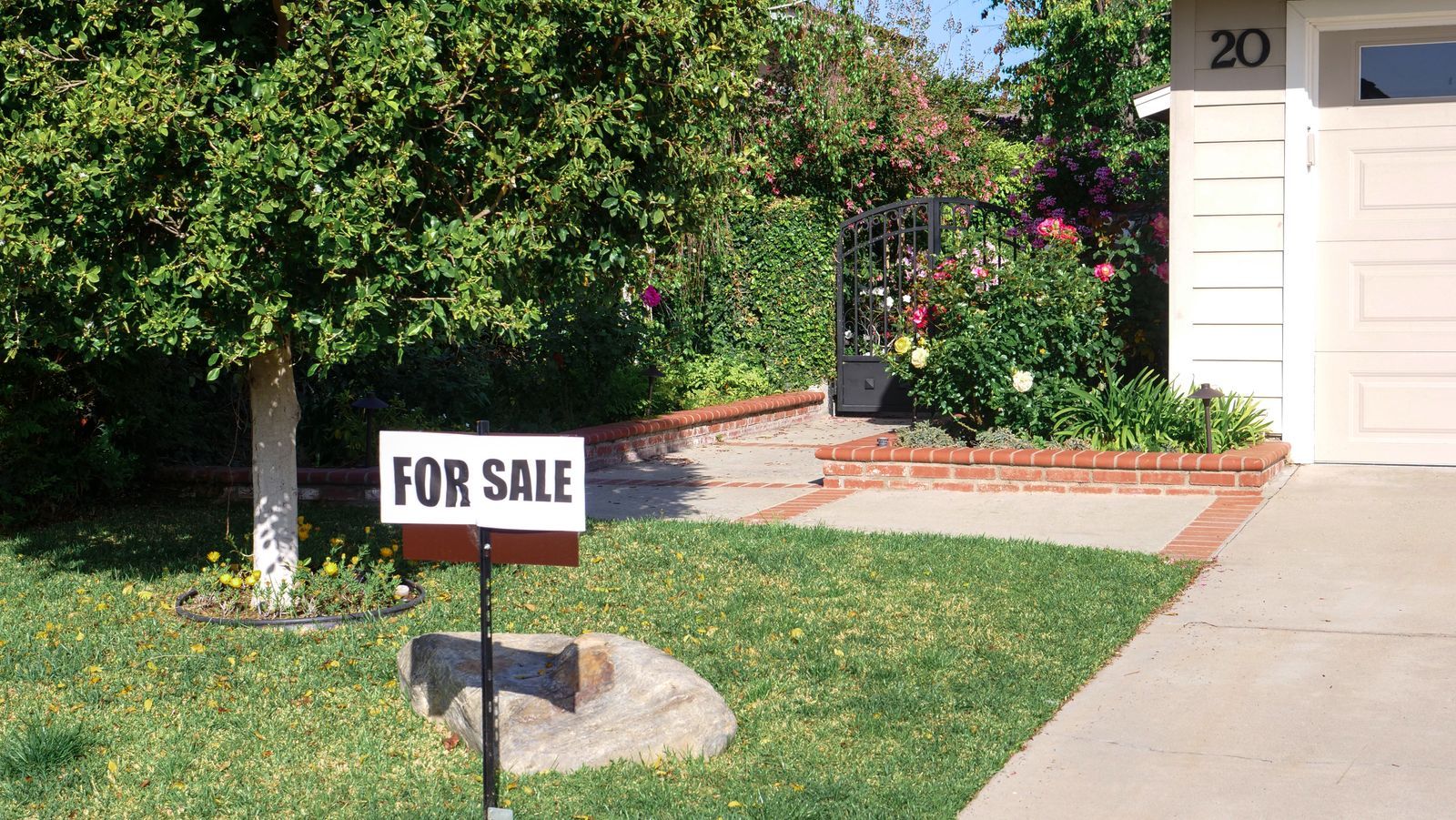 A for-sale sign on a green front lawn outside a home on a bright summer day