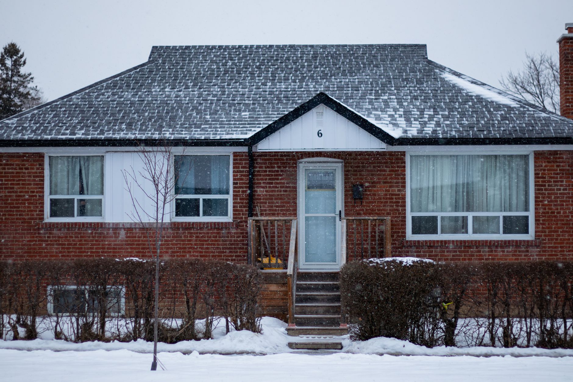 A snow-covered brick home on a quiet Canadian street in winter