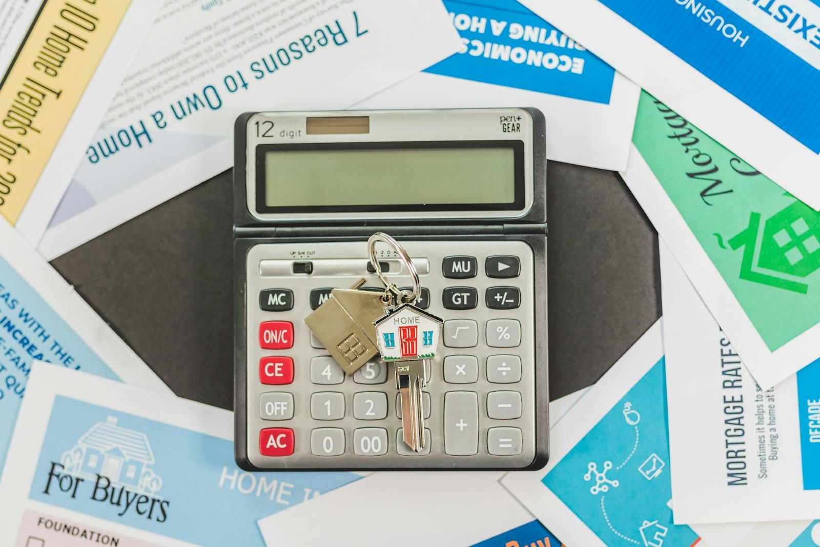 Flat lay of a calculator, house keys, and real estate paperwork on a neutral surface