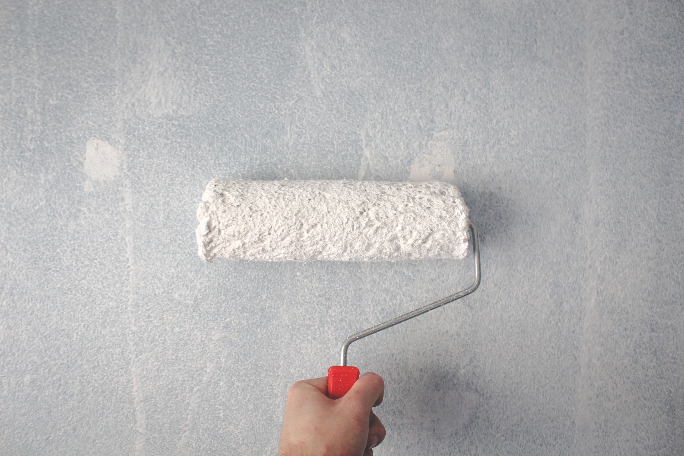 A hand rolling fresh neutral paint onto an interior wall during a pre-sale home refresh